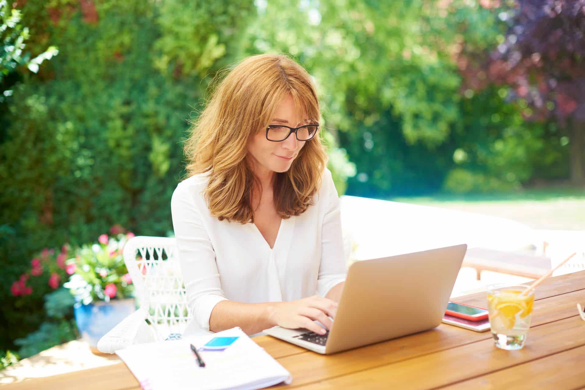 Frau arbeitet konzentriert an einem Laptop in einer grünen Gartenumgebung mit einem Getränk auf dem Tisch, ideal geschützt durch einen Faltpavillon.