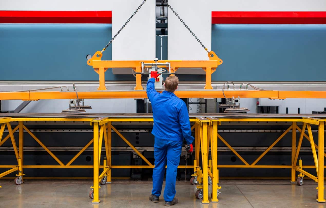 Industriemitarbeiter in blauer Arbeitskleidung bedient einen Elektrokettenzug zum Heben schwerer Lasten in einer modernen Fabrikhalle