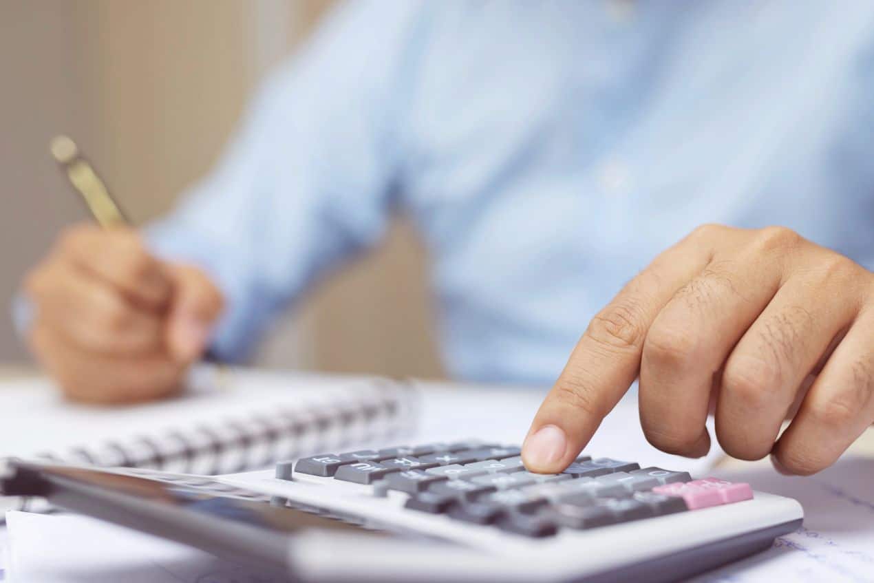 Hand tippt auf Taschenrechner mit Stift und Notizblock im Hintergrund als Symbol für digitale Lohnabrechnung online