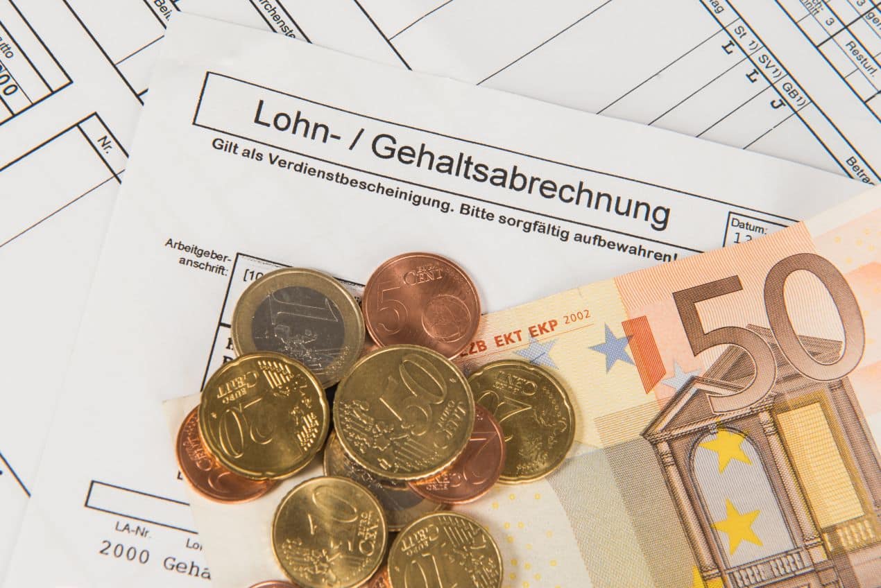 Euromünzen und Geldschein auf Lohnabrechnung als Symbol für Lohnabrechnung online und digitale Gehaltsverwaltung