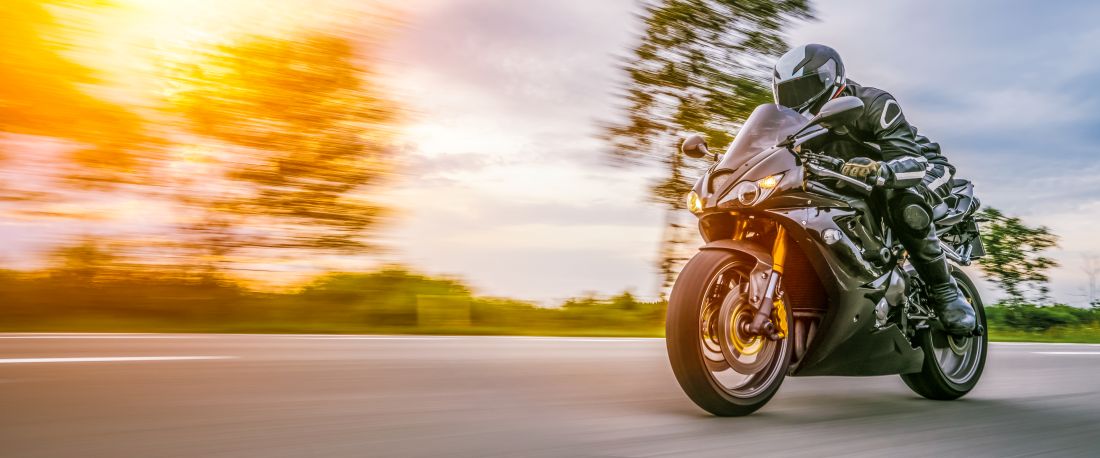motorradfahrer in schutzkleidung faehrt bei sonnenaufgang zur arbeit auf freier landstrasse