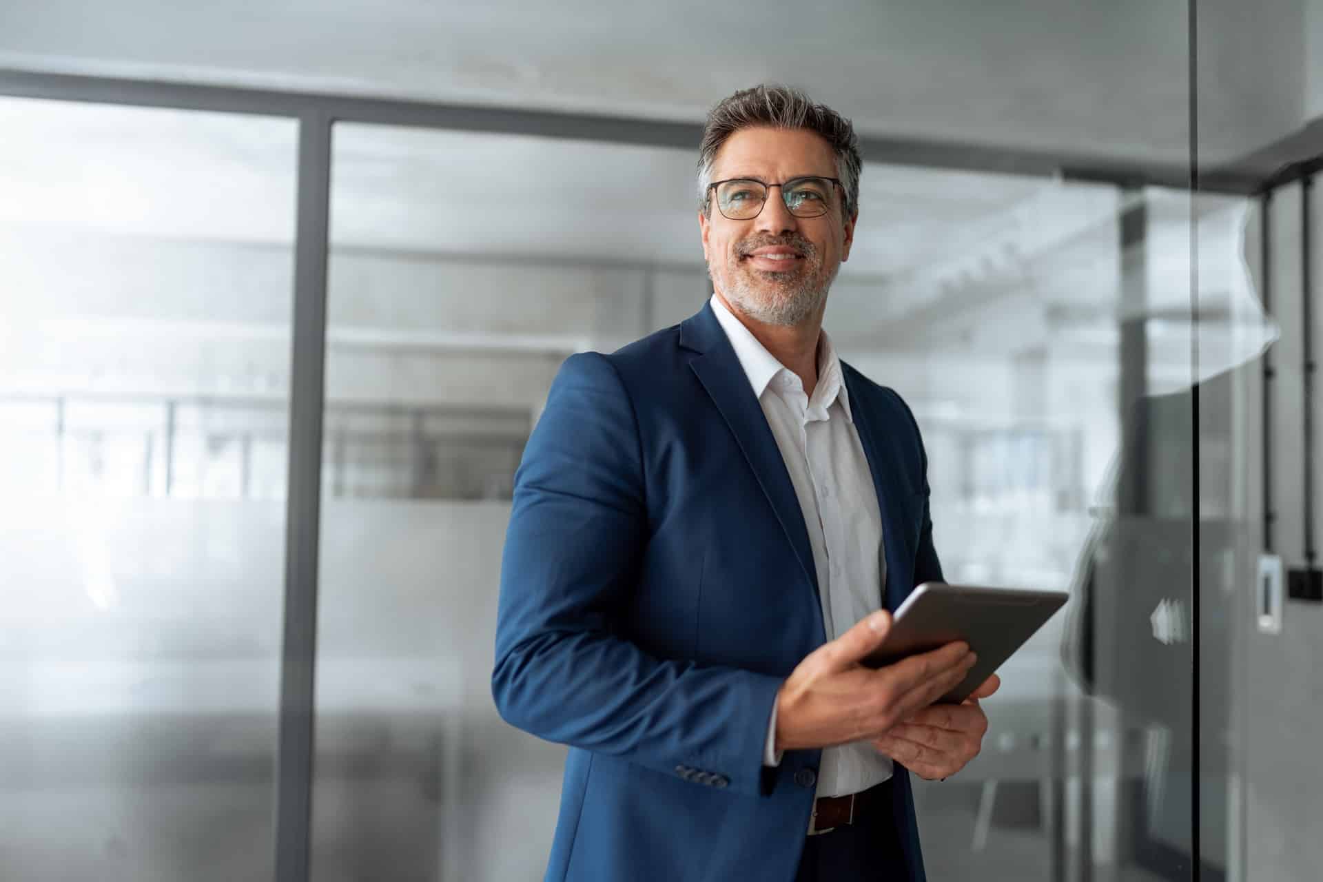 Geschäftsmann mit Tablet steht im Büro und lächelt | Arbeitsschutz E-Learning